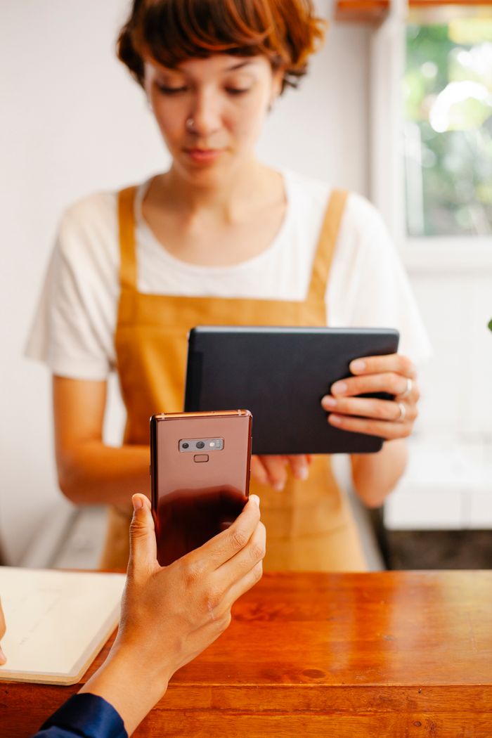 Crop unrecognizable cafeteria employee showing cellphone to female coworker with tablet at counter in daytime